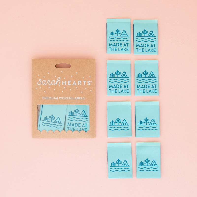 A package of Made at the Lake Sew In Labels next to 8 individual labels on a pink background to show scale and detail.