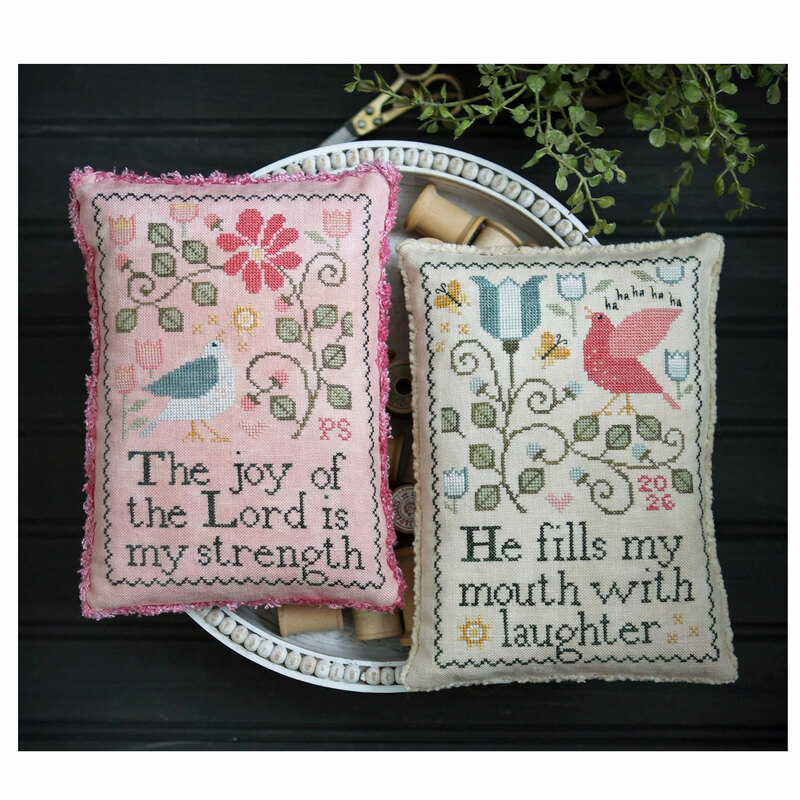 The completed cross stitch finished as a pillow sitting in a wooden bowl surrounded by coordinating décor.