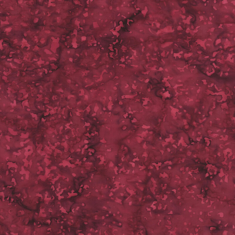 Red batik fabric with a mottled pattern of scattered spots and speckles.