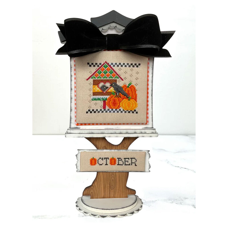 The completed Feathered Friends: October cross stitch project, displayed on a coordinating cross stitch display stand.