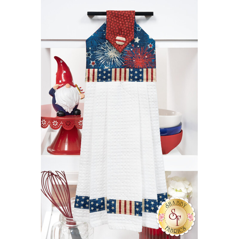 The completed Hanging Towel Kit colored in red, white, and blue fabrics from the American Heartland collection by Northcott Fabrics, hung on a drawer surrounded by coordinating patriotic décor. 