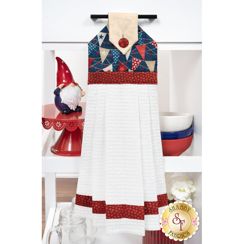 The completed Hanging Towel Kit colored in red, white, and blue fabrics from the American Heartland collection by Northcott Fabrics, hung on a drawer surrounded by coordinating patriotic décor. 