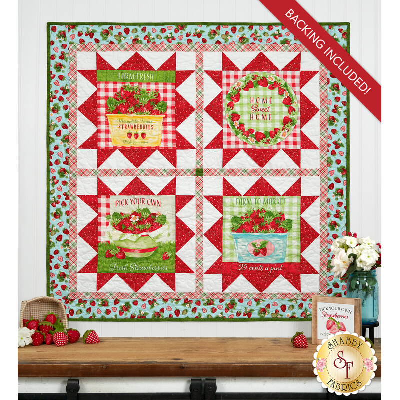The completed Double Geese Wall Hanging, colored in aqua, green, white, and red fabrics from the Berry Besties collection by Henry Glass Fabrics, hung on a white paneled wall and staged with coordinating flowers and décor.