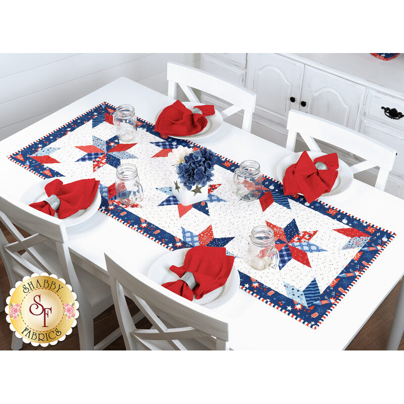 The completed Floating Stars Runner, staged on a white table with red napkins, and glass jars on a white table.