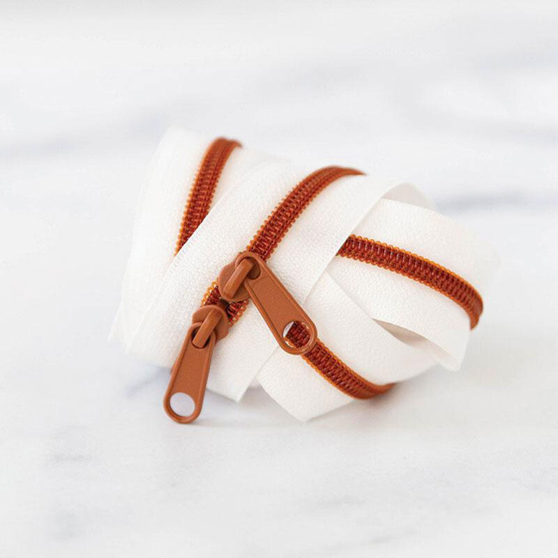 A spool of white zipper tape with brown zippers coiled together on a light surface.