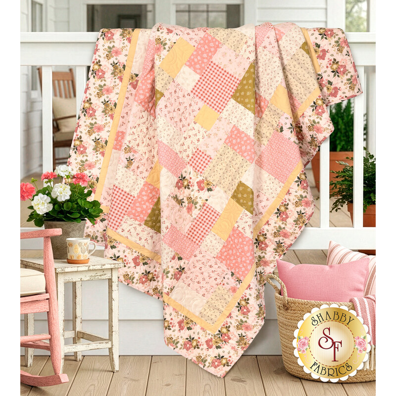 The completed Easy as ABC and 123 Quilt Kit colored in pink, cream, and ocher fabrics from the Renew collection by Riley Blake Designs, artfully draped over a porch railing and staged with coordinating décor.