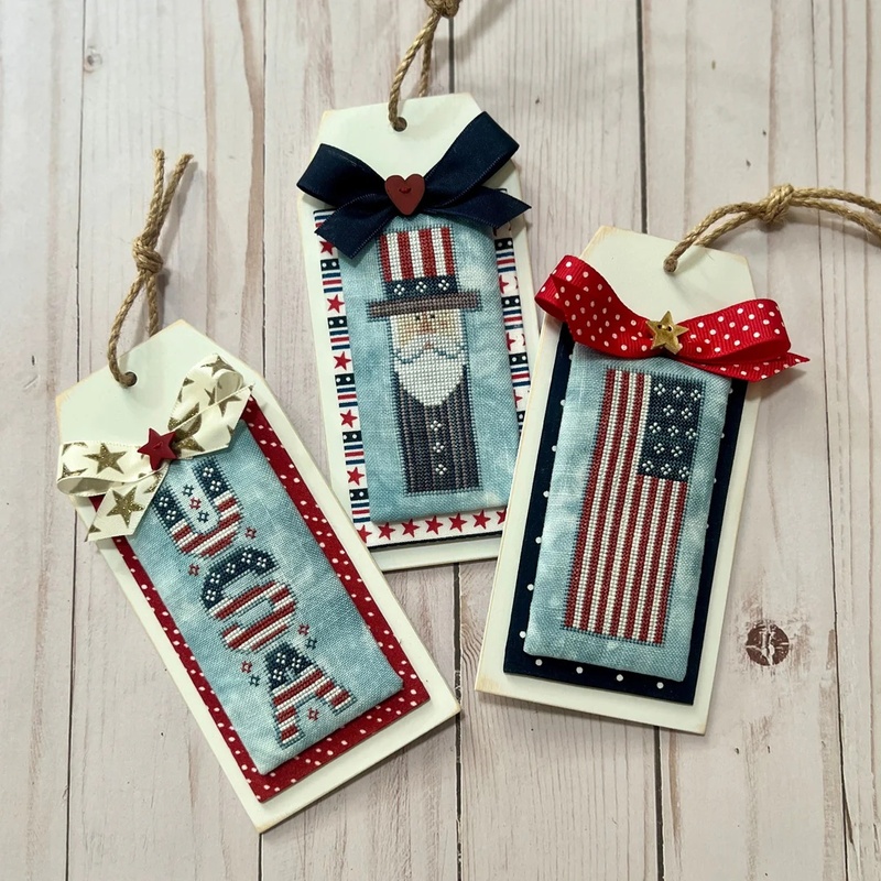 The three completed cross stitch projects, mounted on wooden tags with fabric bow accents.