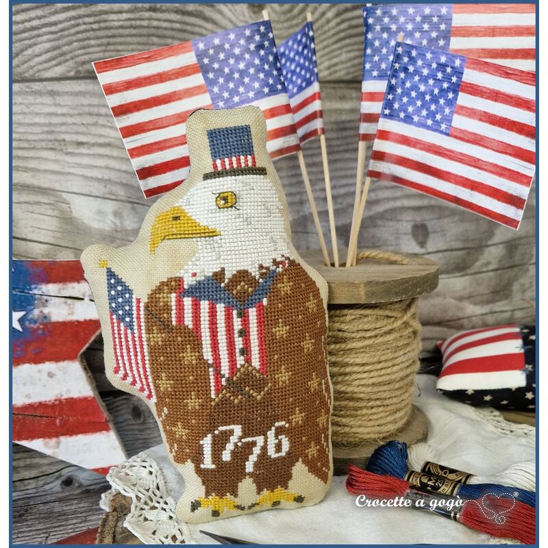 The completed 1776 eagle finished as a pillow, staged with American flags and 1776, surrounded by craft materials