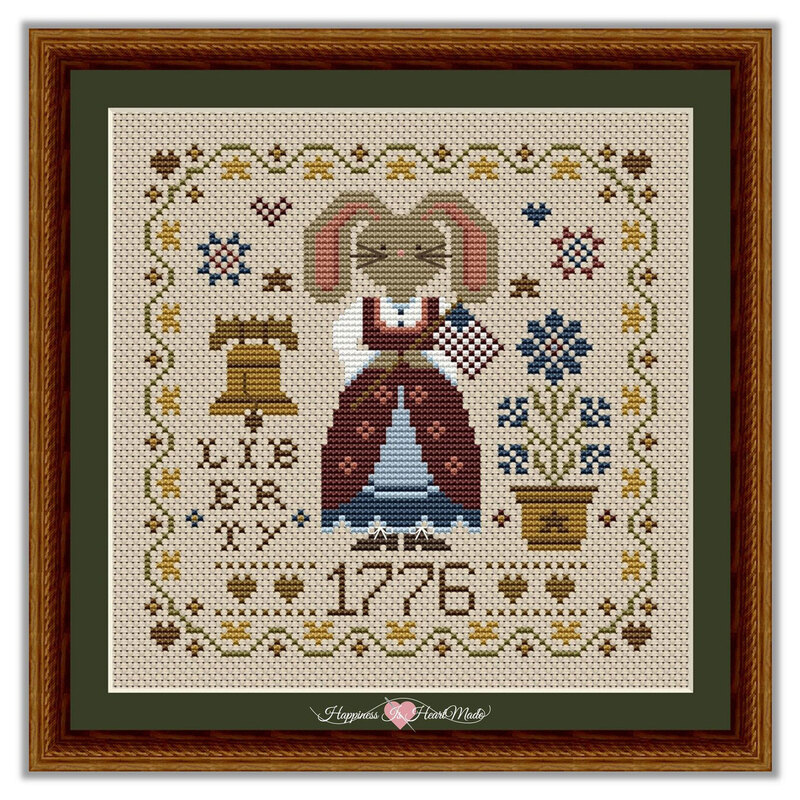 The finished and framed cross stitch project featuring a dressed bunny holding a flag with the liberty bell, 1776, and a potted flower.