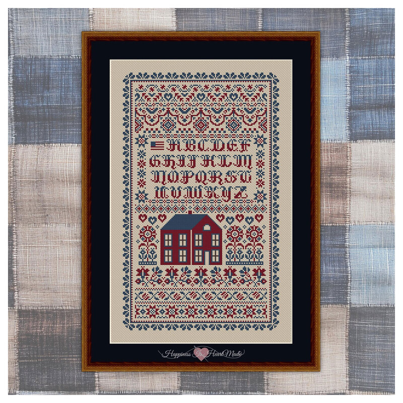 The completed and framed cross stitch project featuring florals, flags, a red house, and the alphabet, on a checkered fabric background.