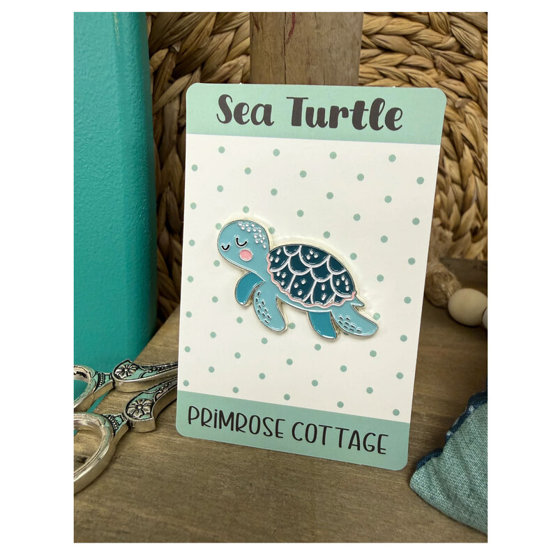 The Sea Turtle needle minder, stood up on a table with embroidery scissors, a spool of thread and coordinating décor.