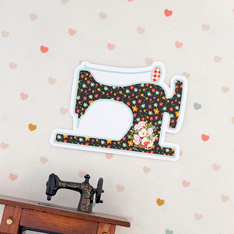 A floral-patterned decorative sewing machine sticker hangs on a wall with a heart motif.