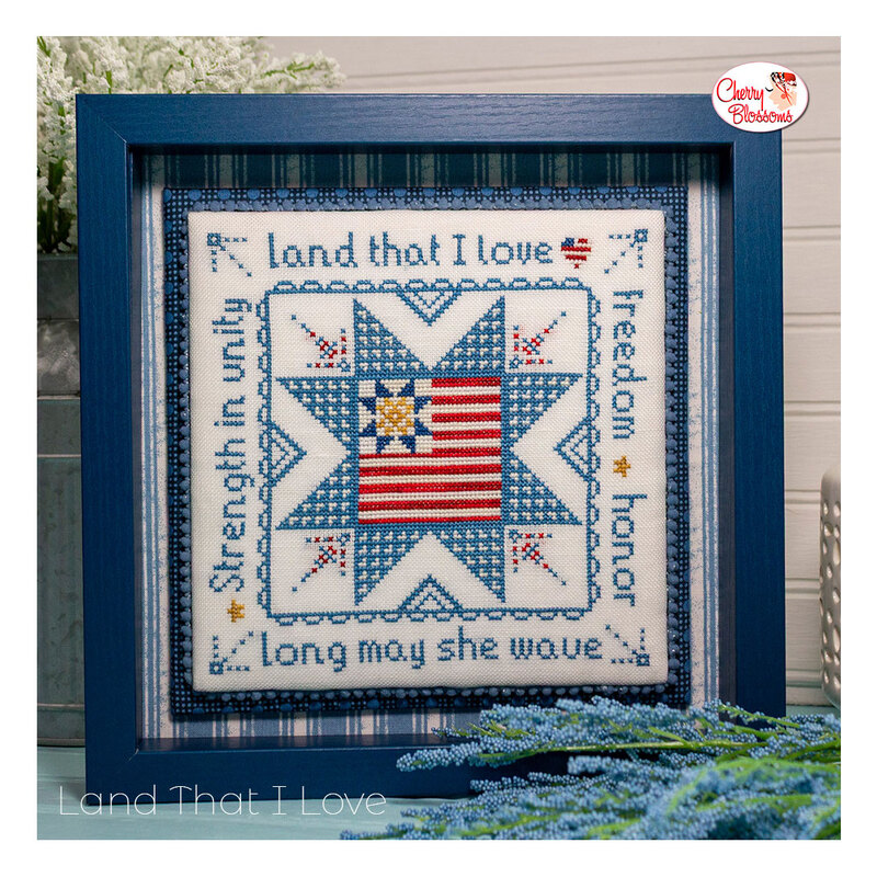 The completed Land That I Love cross stitch pattern framed and surrounded by coordinating décor. 