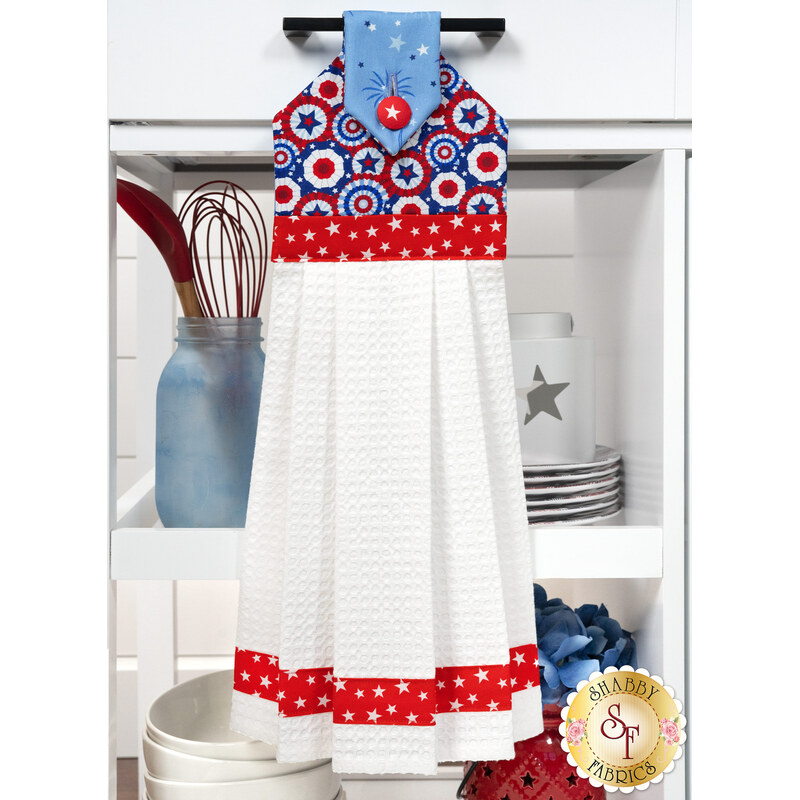 The completed Hanging Towel Kit colored in red, white, and blue fabrics from the Celebrate The USA collection from Benartex, hung on a drawer surrounded by coordinating patriotic décor. 