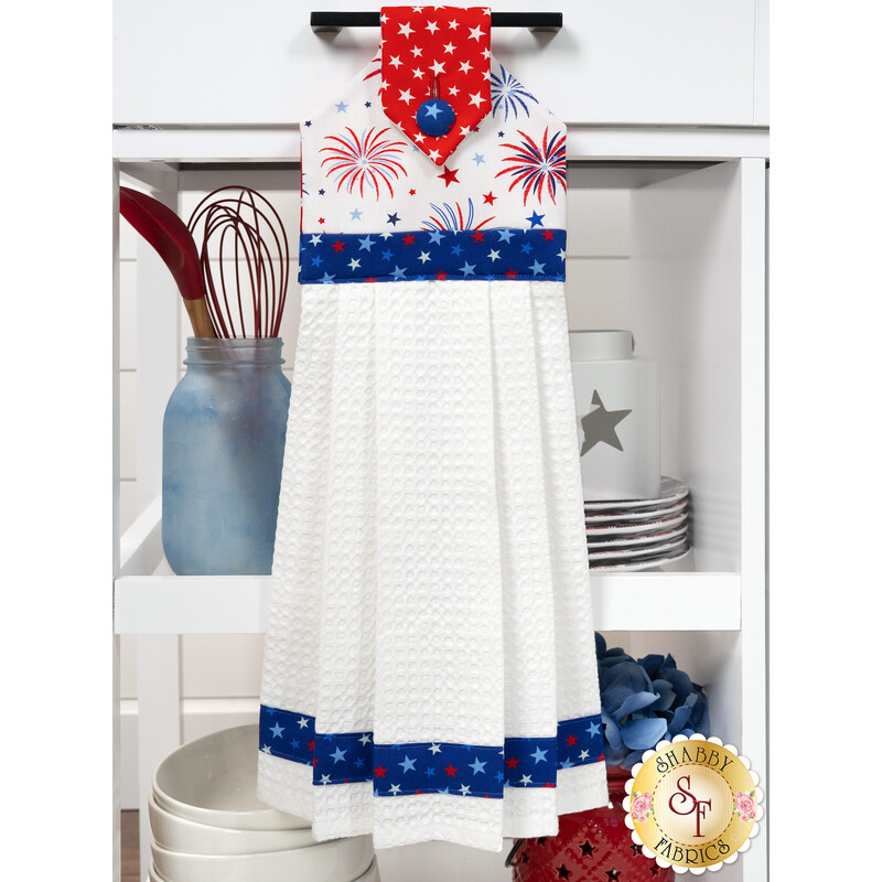 The completed Hanging Towel Kit colored in red, white, and blue fabrics from the Celebrate The USA collection from Benartex, hung on a drawer surrounded by coordinating patriotic décor. 
