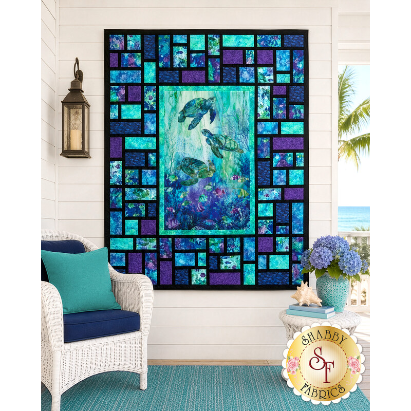 The completed Stained Glass Panel Quilt II, colored in bold cyan, blue, violet, and black fabrics from the Coral Reef collection by Northcott Fabrics, staged on a seaside porch with coordinating décor.