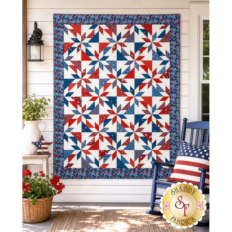 The finished Playing Favorites Quilt, colored in red, white, and blue fabrics from the Front Porch Charm collection, staged on a white porch wall with coordinating décor.