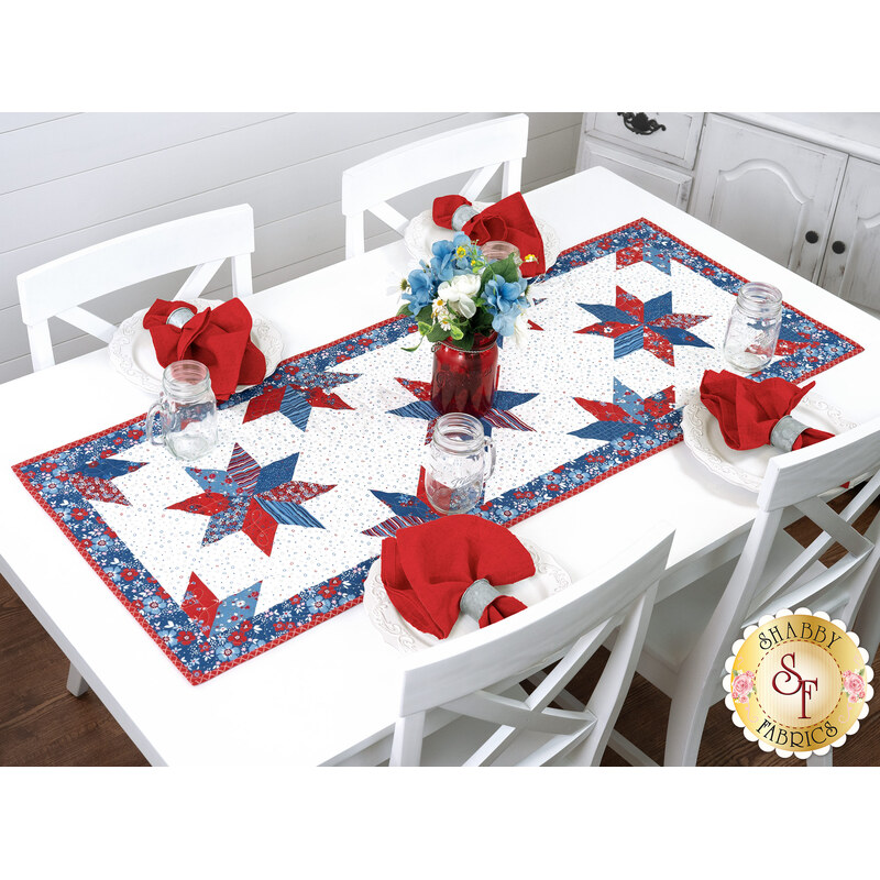 The completed Floating Stars Runner, staged on a white table with red napkins, and glass jars on a white table.