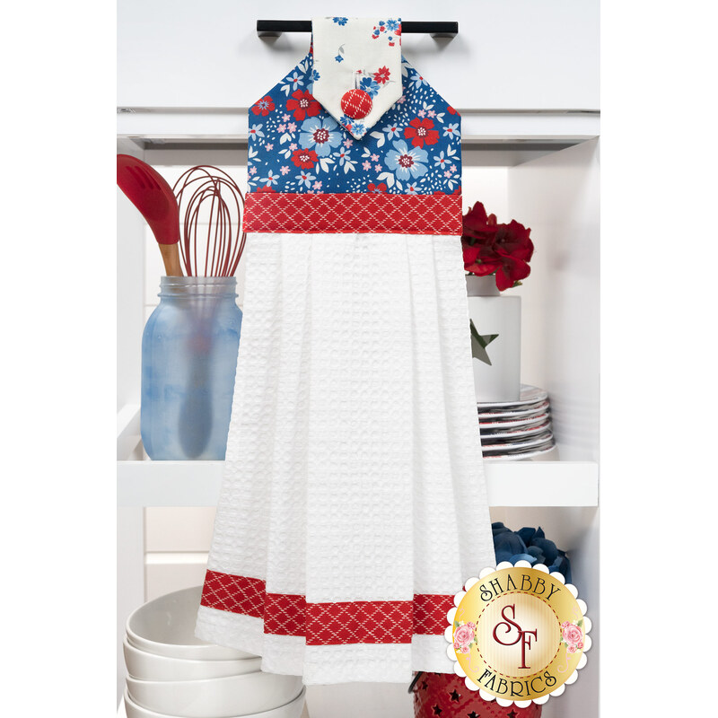 The completed Hanging Towel Kit colored in red, white, and blue fabrics from the Front Porch Charm collection from Blank Quilting, hung on a drawer surrounded by coordinating patriotic décor. 