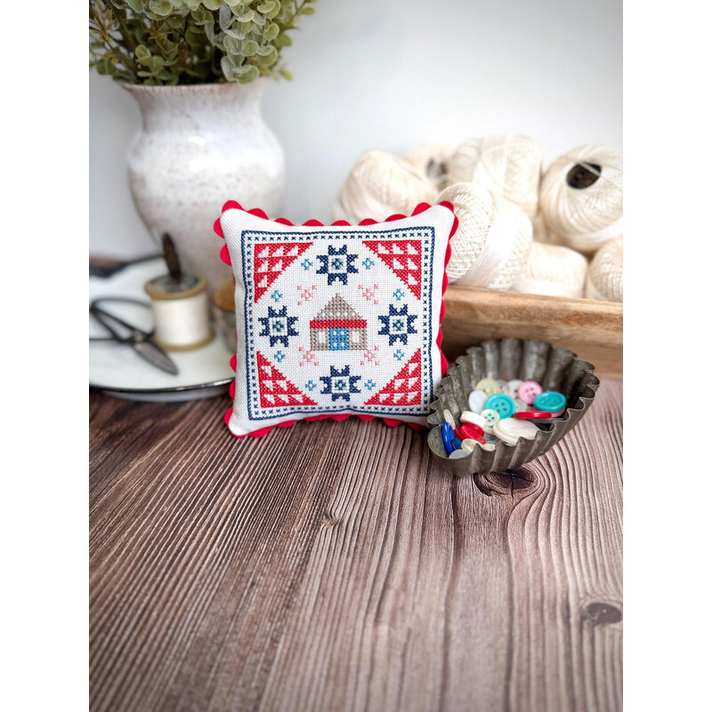Decorative embroidered cushion on a wooden table, with a bowl of colorful buttons and yarn in the background.