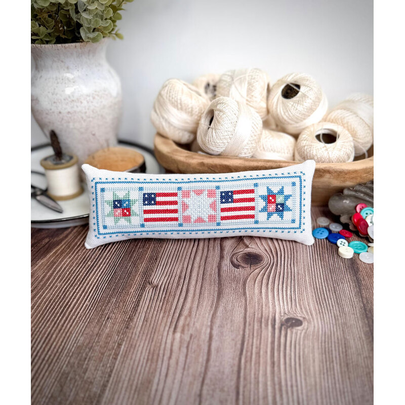 A decorative pillow featuring stars and stripes, placed on a wooden surface.