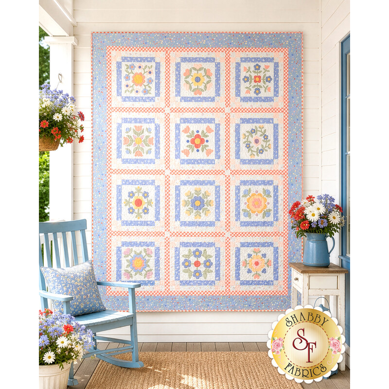 The completed Baltimore Quilt colored in soft blues, peach pinks, and cream fabrics from the Pastel Prairie collection from Moda Fabrics, staged on a white porch with coordinating décor.