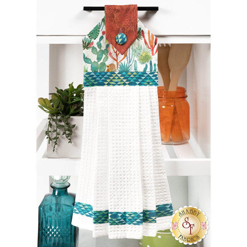 A head on shot of the completed white Hanging Towel, colored in fabrics from the Desert Dreams collection by Maywood Studio, hung on kitchen drawer and staged with coordinating décor.