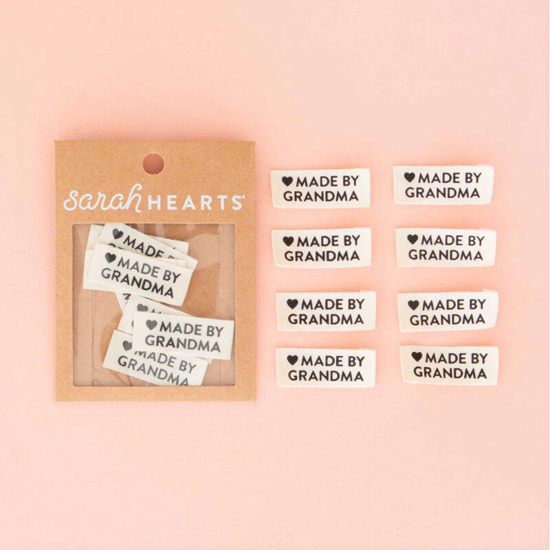 A package of Made by Grandma Sew In Labels next to 8 individual labels on a pink background to show scale and detail.