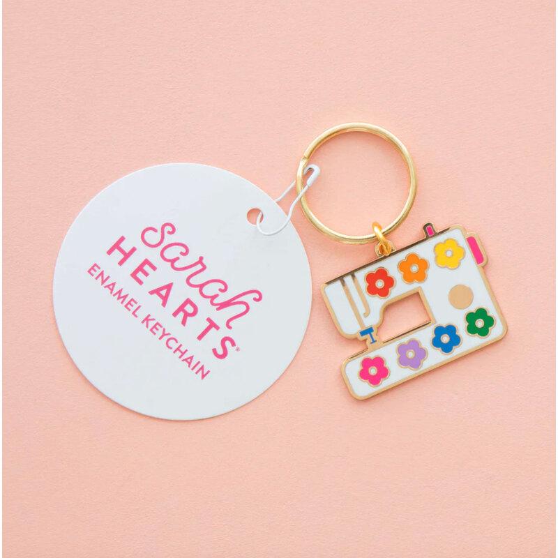 Enamel keychain featuring the design of a sewing machine, isolated on a pink background.