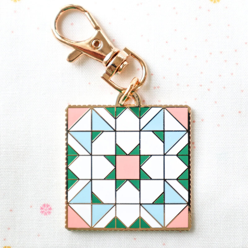 Gold keychain charm shaped like a quilt block.