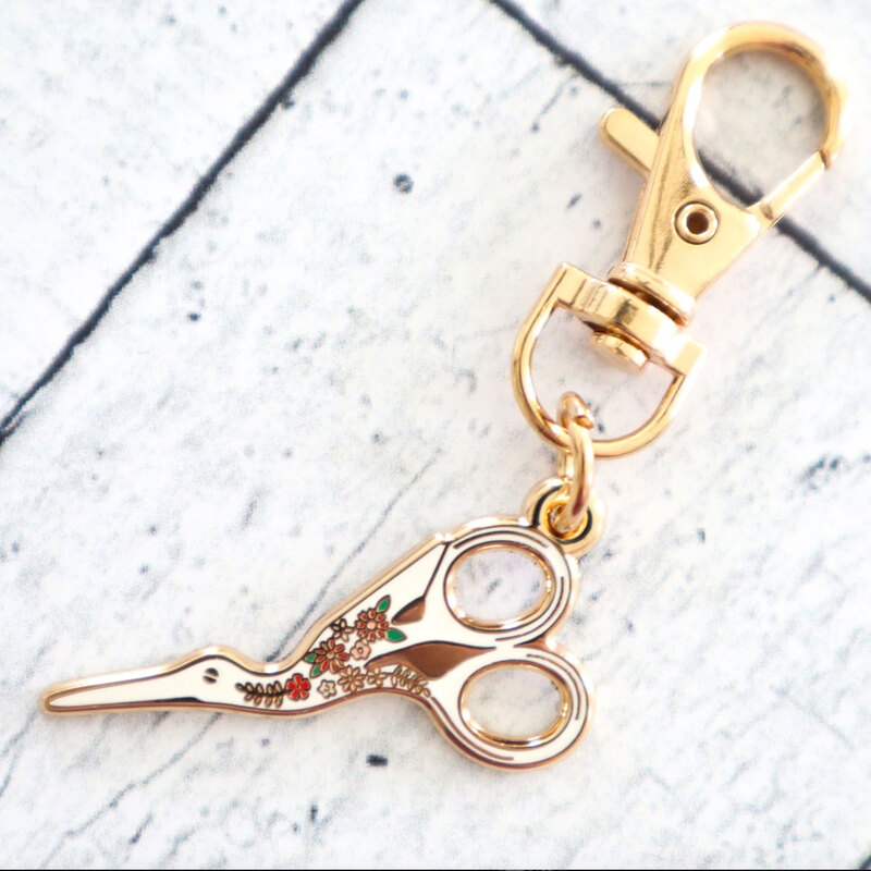 Gold keychain charm shaped like scissors.