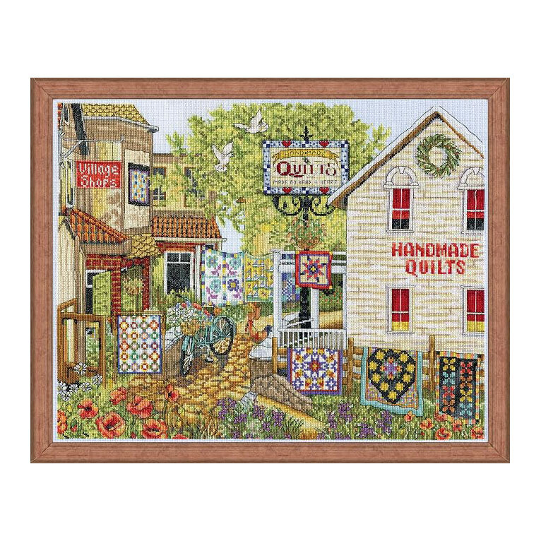 The cross stitch project featuring village shops with hanging quilts and planted flowers along a cobbled street, finished with a wooden frame.