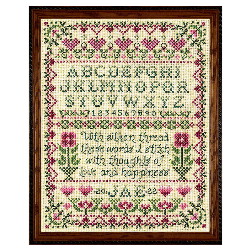 Framed cross stitch project featuring a floral border, the alphabet, and a quote, in pink and green thread.
