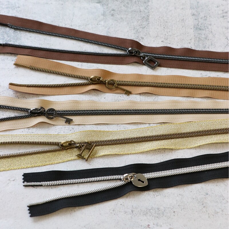 Five zipper pieces in various colors arranged horizontally, showing their coordinating novelty zipper pulls.