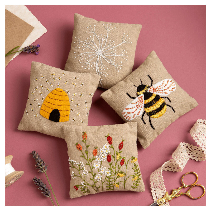 The completed Linen Lavender Bags Embroidery Kit resting on a pink background and surrounded by coordinating décor. 