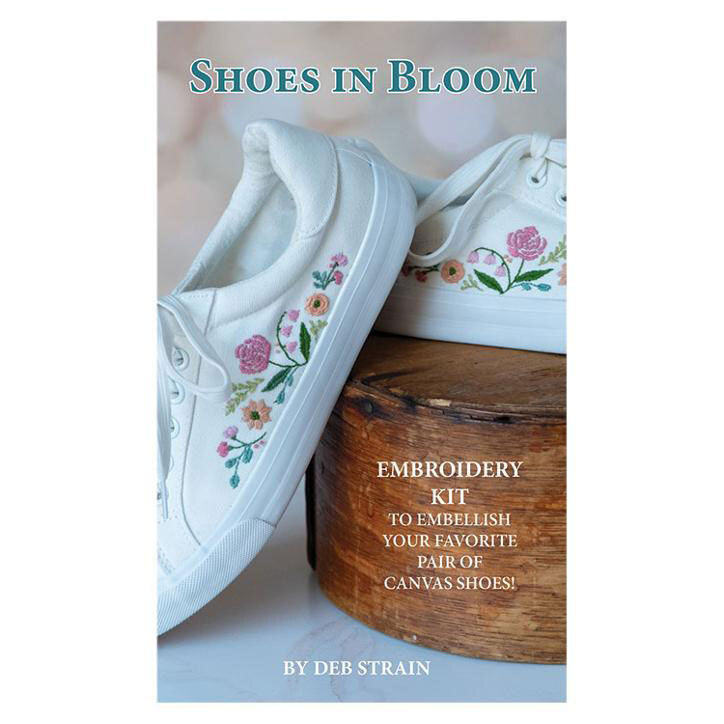 The cover of the Shoes In Bloom embroidery kit displaying the completed project, a white canvas sneaker with the floral embroidery design in hues of pink, peach, blue, and green.