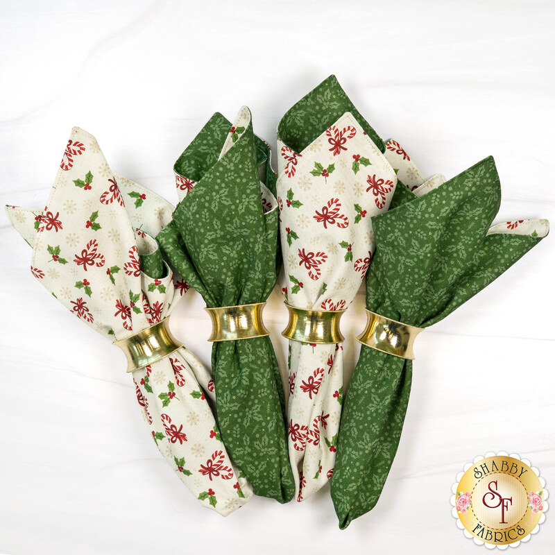 The four completed cloth napkins, colored in cream, green, and red fabrics from the Peppermint & Pine collection by Marcus Fabrics, staged on a white marbled background.