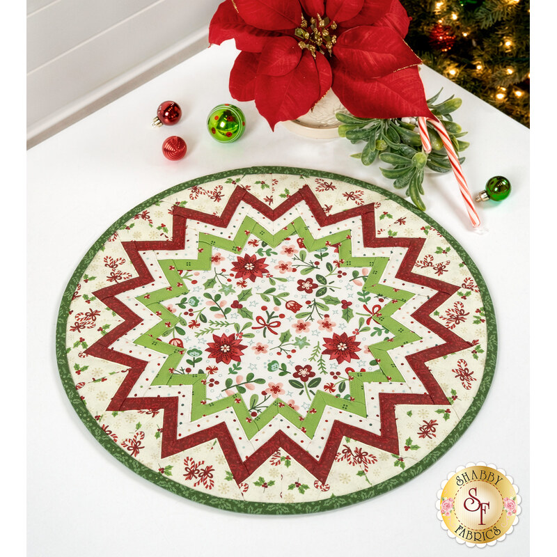 The completed Point of View Folded Star Table Topper, colored in bright green, red, and cream fabrics from the Peppermint & Pine collection, staged on a white table with coordinating décor.