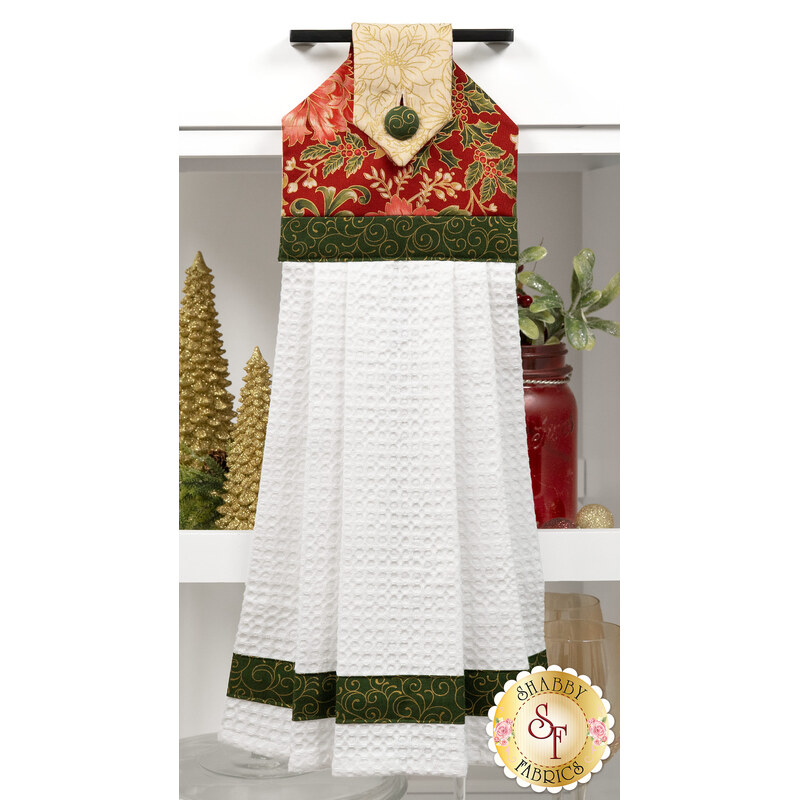 A head-on shot of the completed red Hanging Towel, colored in cream, green, and red metallic fabrics from the Merry Manor Metallic 2025 collection by Moda Fabrics, hung on kitchen drawer and staged with coordinating décor.