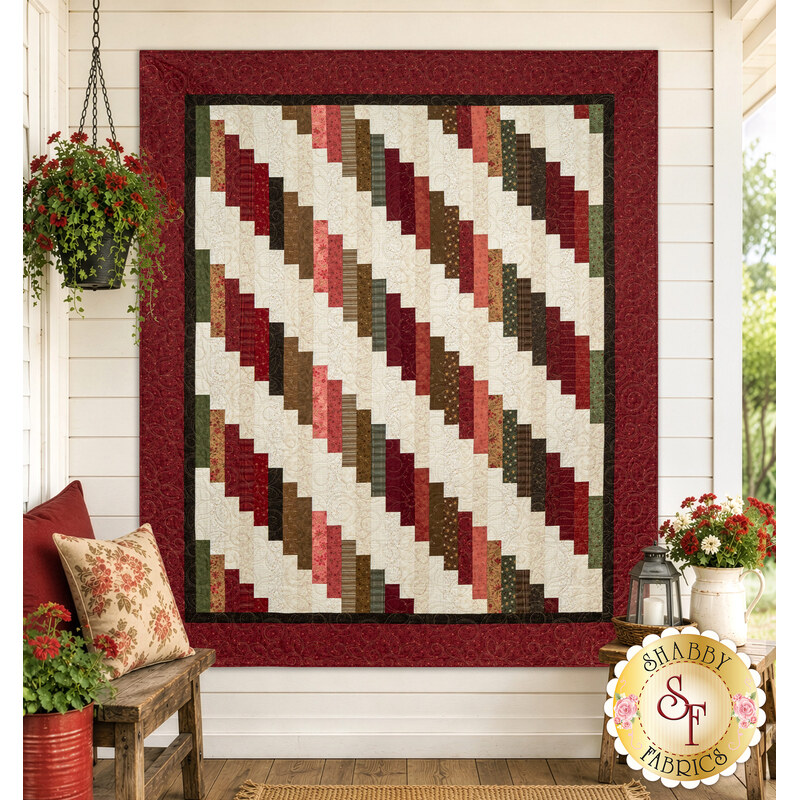 The completed 28th Floor Quilt colored in cream, red, pink, and green fabrics from the Hearth & Home collection by Henry Glass Fabrics, staged on an off-white porch wall with coordinating furniture and décor.