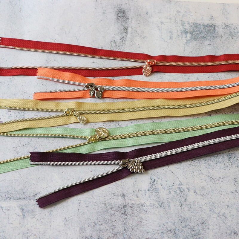 Five zipper pieces in various colors arranged horizontally, showing their coordinating novelty zipper pulls.