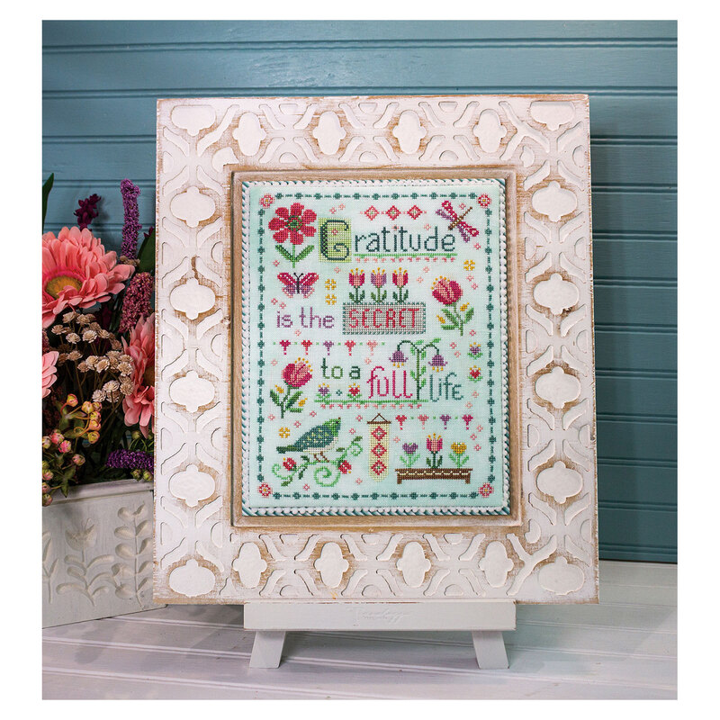 A decorative framed cross stitch project featuring the words "Gratitude is the secret to a full life" with florals, hearts, birds, butterflies, and dragonflies.