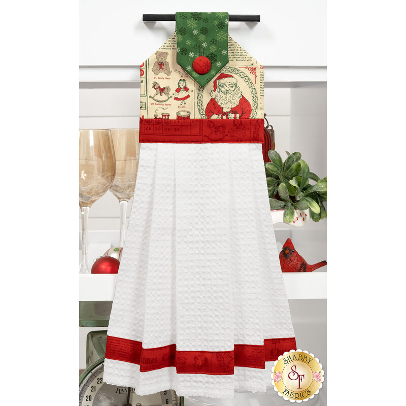 A head on shot of the completed cream Hanging Towel, colored in fabrics from the Holiday Cheer collection by Moda Fabrics, hung on kitchen drawer and staged with coordinating décor.