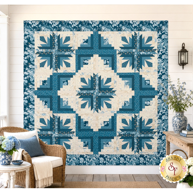 The completed Cactus in the Cabin quilt, colored in cream and blue fabrics from the Special Delivery collection by Andover Fabrics. The quilt is hung on a cream shiplap wall and staged with coordinating furniture and décor.