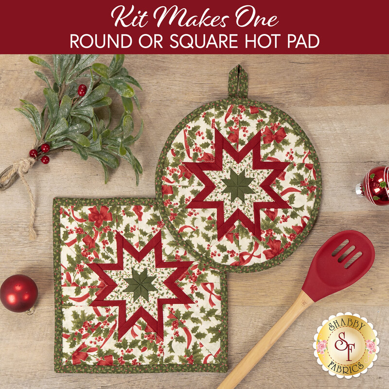 The two completed Folded Star Hot Pads colored in cream, red, and green fabrics from the Candlelight Christmas collection by Moda Fabrics, slightly overlapping each other and staged on a wood table with coordinating décor.