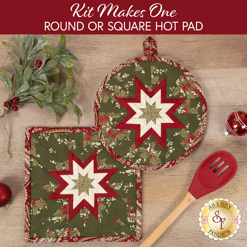 The two completed Folded Star Hot Pads colored in cream, red, and green fabrics from the Candlelight Christmas collection by Moda Fabrics, slightly overlapping each other and staged on a wood table with coordinating décor.