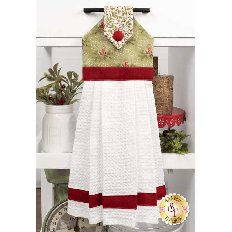 The completed Hanging Towel colored in cream, red, and green, fabrics from the Candlelight Christmas collection by Moda Fabrics, staged on a kitchen drawer with coordinating decor.