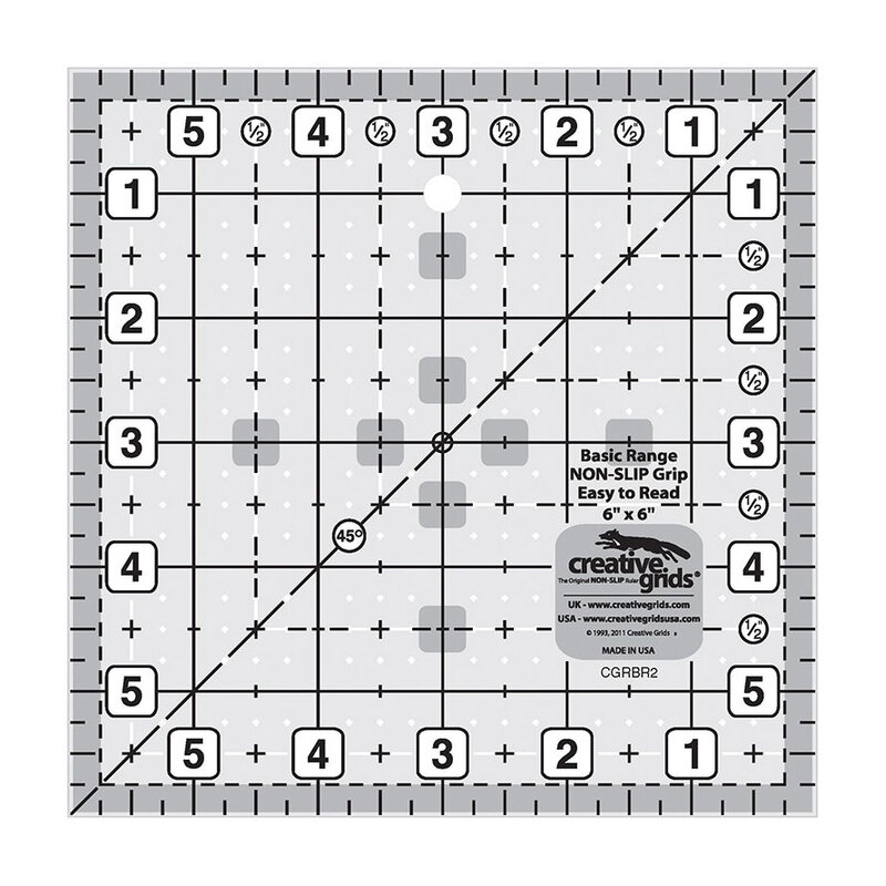 A square quilting ruler marked with grid lines up to 6", numbers, and a central hanging hole.