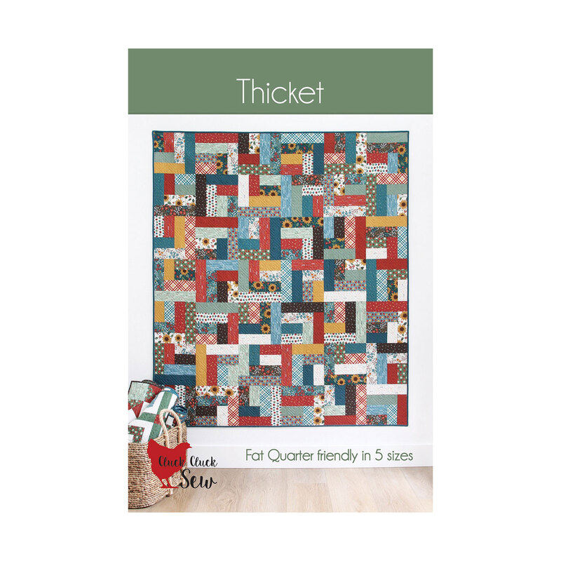 The front of the Thicket pattern featuring a multicolor quilt with a rotating strip piece block pattern hung on a white wall.