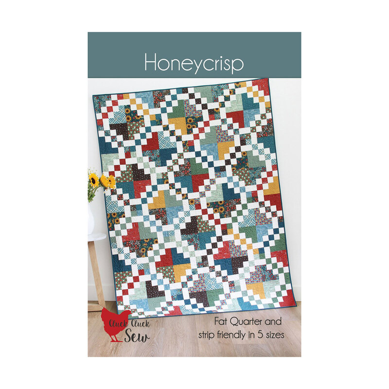 The front of the Honeycrisp pattern featuring a multicolor quilt with an Irish chain block pattern hung on a white wall.